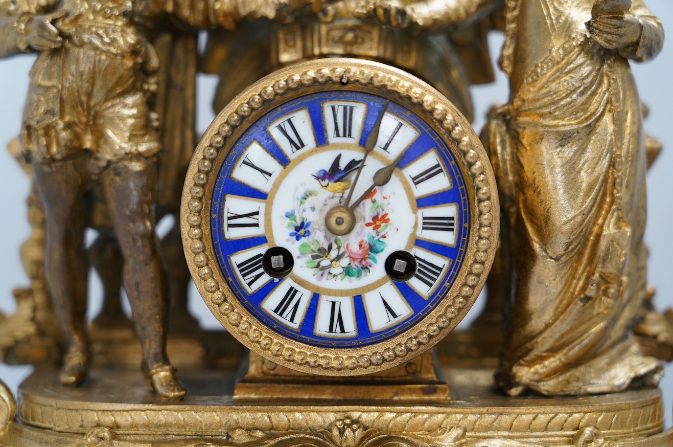 A large gilt metal figural mantel clock with floral porcelain dial and panels, under a glass dome, 52cm high (including stand). Condition - fair, not tested as working